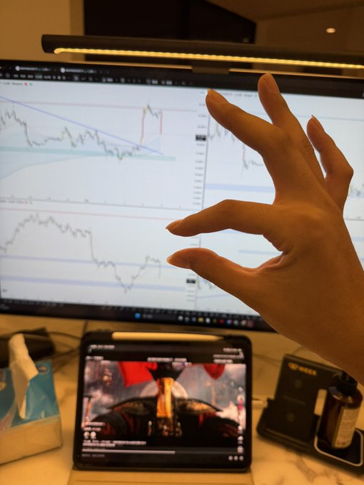 A hand gestures toward a trading screen displaying candlestick charts, with a tablet below showing an F1 race—symbolizing "拿捏" (having things firmly under control) across both high-stakes financial markets and motorsport.
