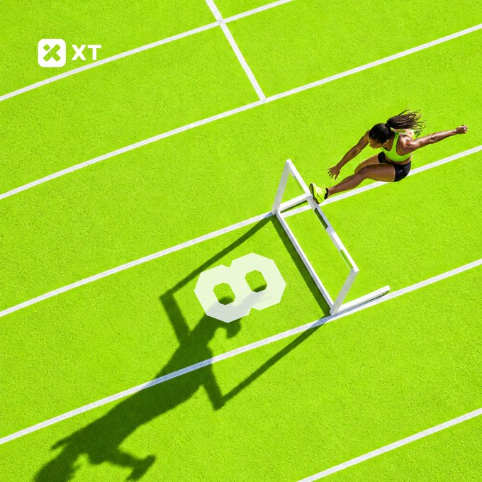 A female athlete in neon green athletic wear leaps over a white hurdle on a vibrant green track, with the number "8" painted on the lane beside her casting a bold shadow. The image visually echoes the post's "8 years built" and "NeXT 8" theme, with the "XT" logo in the corner reinforcing the brand's milestone celebration and call to shape its future.