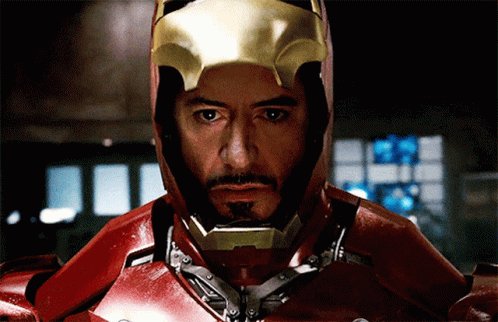 urnacle, the Iron Man character from "The Avengers", stands against a dark background with a blue window and a red brick wall.