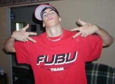 The image shows a young man wearing a white cap, glasses, a chain, and a red "FUBU TEAM" t-shirt, posing with both hands extended outward. Given the post context referencing "ENS" (a family/crew name), the caption likely represents a casual street-style portrait tied to group identity or affiliation.
