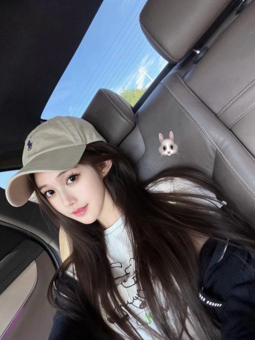 A young woman wearing a beige Polo Ralph Lauren cap takes a selfie inside a car on a sunny day, with a small bunny emoji sticker decorating the leather headrest behind her. The image pairs with the caption "周末去哪玩儿？" (Where to go this weekend?) to suggest a casual, ready-for-adventure vibe perfect for planning weekend outings.