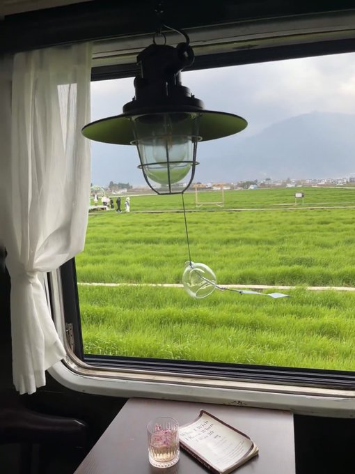 A vintage-style lantern hangs in a train window, framing a scenic view of lush green rice fields and distant mountains, while a glass and menu rest on the table below.

The image appears to share little direct connection to the post's discussion of "AI+Crypto" and crypto community divisions; rather, its peaceful, contemplative setting of a moving train journey may serve as a metaphor for the crypto landscape in transition—gliding forward through uncertain terrain with both innovation and ambiguity ahead.