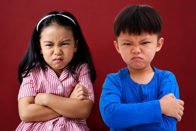Two children—one girl in a red-and-white striped dress and one boy in a blue shirt—stand with arms crossed and angry, pouting expressions against a red backdrop. Their frustrated faces visually mirror the post's tone of regret and frustration toward parents who missed buying XRP at a low price.
