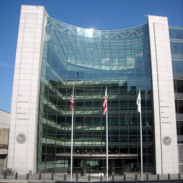 The U.S. Securities and Exchange Commission (SEC) headquarters is shown, a modern glass-fronted building with three flags flying at the entrance, symbolizing regulatory developments in financial markets. This image directly relates to the post's discussion of potential SEC actions enabling 24/7 tokenized stock trading and its implications for projects like $STONKBROKER.