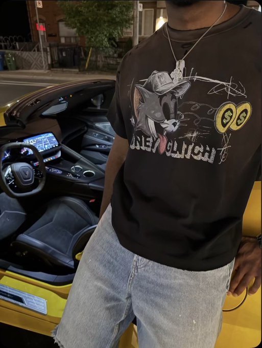A person wearing a black Bugs Bunny 'Hell Yeah' graphic t-shirt and distressed jeans, standing beside a yellow Chevrolet Corvette with its door open.