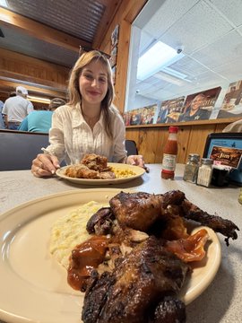 iced tea and a plate of food are on the table, with a woman seated at the table in front of them.