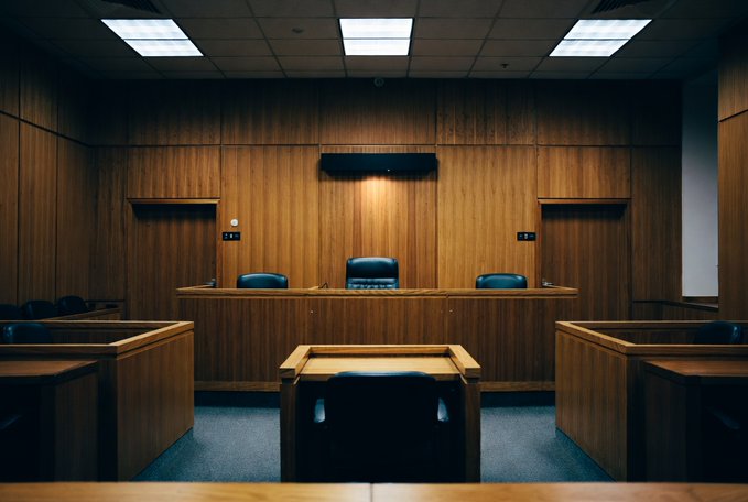 An empty courtroom with wooden paneling, judge's bench, and witness stand sits in quiet contrast to the alleged $20 million crypto fraud scheme involving Sioux Falls investor Benjamin Paul Wiener, who faces 29 counts and a Sept. 15 trial date. The vacant scene underscores the gravity of the pending proceedings ahead.