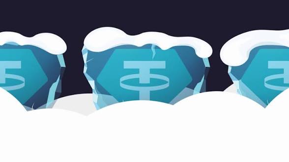 Three blue Tether (USDT) tokens sit partially buried in snow, symbolizing the freezing of USDT on 131 TRON wallets linked to ISIS-K by OFAC's sanctions.
