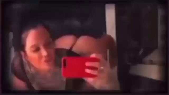 The image shows a woman taking a selfie with her phone, holding it up to take a picture of herself. She appears to be wearing a black shirt while capturing the moment. The photo has been edited or filtered, giving it an unusual appearance that includes text such as "bitcoin bitcoin". This could indicate that the photo is related to Bitcoin, possibly being used for sharing on social media platforms or other online communities.