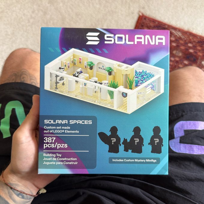 A person wearing Solana-branded shorts holds up a "Solana Spaces" LEGO set box (387 pieces) featuring a custom mystery minifigure, showcasing their Solana-themed merchandise collection as a flex.