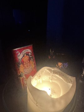 A dimly lit, nighttime scene showing a candle lit inside a paper bag next to an unopened package of Oreo cookies.