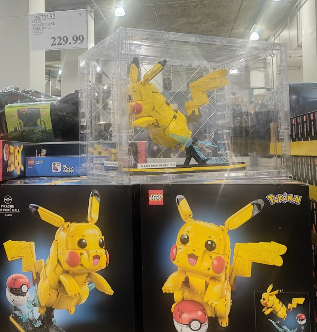 A LEGO Pokémon Pikachu and Poké Ball set (#2672152) displayed in a glass case at a store, with multiple product boxes visible and a price tag reading "229.99".