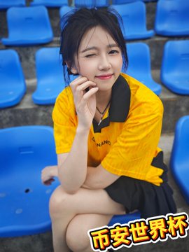 The image features a woman sitting on blue chairs, wearing a yellow shirt with black text that says "Nan" on it. The woman has her hand on her face as she looks at the camera. There are also blue chairs surrounding her, indicating that this might be an event or gathering taking place in a room filled with seating arrangements.