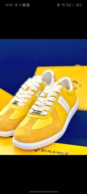 A pair of yellow and white sneakers with 'BINANCE' branding on the tongue tags, displayed on a blue and yellow Binance-branded box.
