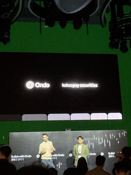 A photograph taken from an audience perspective at a conference showing two speakers on stage with a large screen behind them displaying the logos 'Ondo' and 'kakaopay securities'.