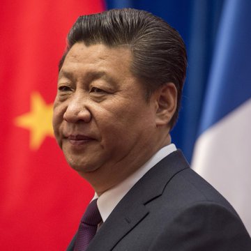 The image features a man wearing a suit and tie standing next to a flag with China written on it. The man appears to be smiling for the camera while posing against this backdrop. In the background of the image, there are three flags - one representing China, another representing France, and the third representing Germany. These flags create an atmosphere of international relations and cooperation among nations.