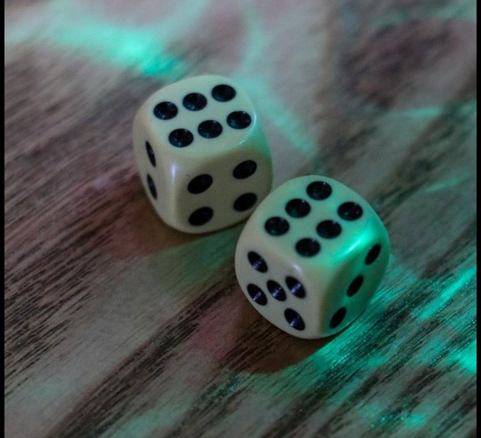 Two white dice with black pips rest on a wooden surface under teal-green lighting.