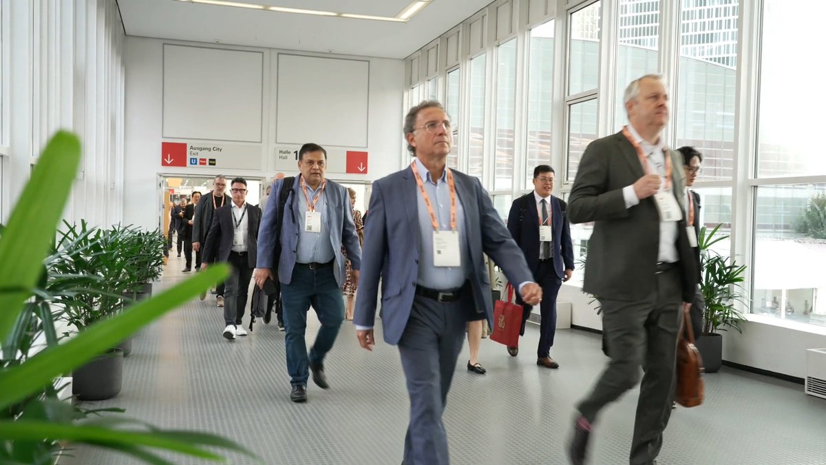 A group of business-attired attendees with orange lanyards walk through a sunlit convention hall corridor toward "Halle 1.1" with directions to "Ausgang City Exit," appearing to head toward a major industry event likely connected to blockchain and cryptocurrency discussions such as Chainlink ($LINK).

Note: The image itself contains no visible reference to Chainlink, LINK, or any ticker — the connection is only implied by the accompanying post's hashtags and ticker, suggesting the photo may be from a conference where Chainlink-related announcements or discussions took place.