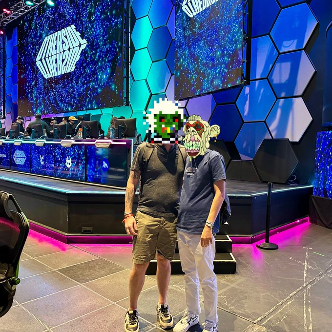 Two people pose for a photo at what appears to be the 'Riverside Aalborg 2025' esports tournament, with their faces covered by pixel art/emoji stickers, standing in front of a stage with hexagonal backdrops and blue lighting.