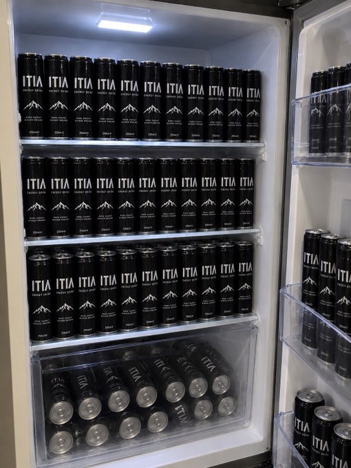 An open refrigerator is fully stocked with rows of black "ITIA Energy Drink" cans on every shelf and in the door, visually capturing the humor of being "addicted" to ITIA.