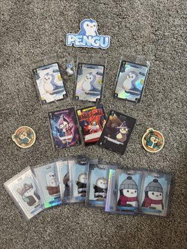 A collection of Pudgy Penguins trading cards and figures, including a 'PENGU' sticker, displayed on a gray carpet.