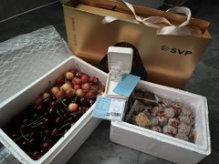 The image features a white box with a gold ribbon, containing various items such as cherries, a ring, and possibly other small objects. The box appears to be filled with cherries, which are placed next to each other. A silver ring is also present in the box along with some other small items. The post includes text that reads "SVP" and "x1".