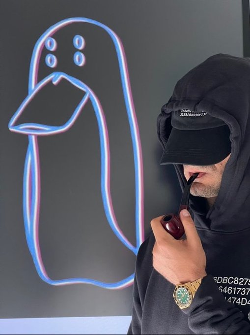 A man wearing a black hoodie and cap smokes a pipe next to a neon sign shaped like a bird, with a gold watch visible on his wrist.