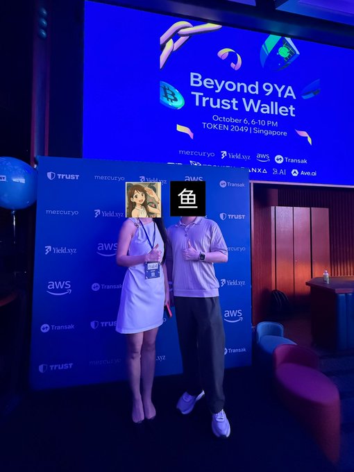 A couple poses in front of a step-and-repeat banner at the "Beyond 9YA Trust Wallet" event on October 6, 6-10 PM at TOKEN 2049 Singapore, with logos for Trust, mercuzyo, YieldLyX, and AWS in the backdrop.