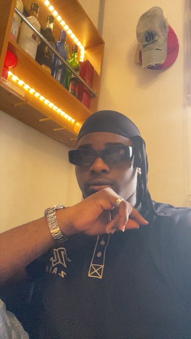 A man wearing sunglasses, a black durag, and a silver watch poses thoughtfully in front of a bar shelf lined with bottles, with a cap featuring the "CryptoRank" logo mounted on the wall behind him—visually tying into his post about using CryptoRank as a Web3 research tool for finding projects and job opportunities.