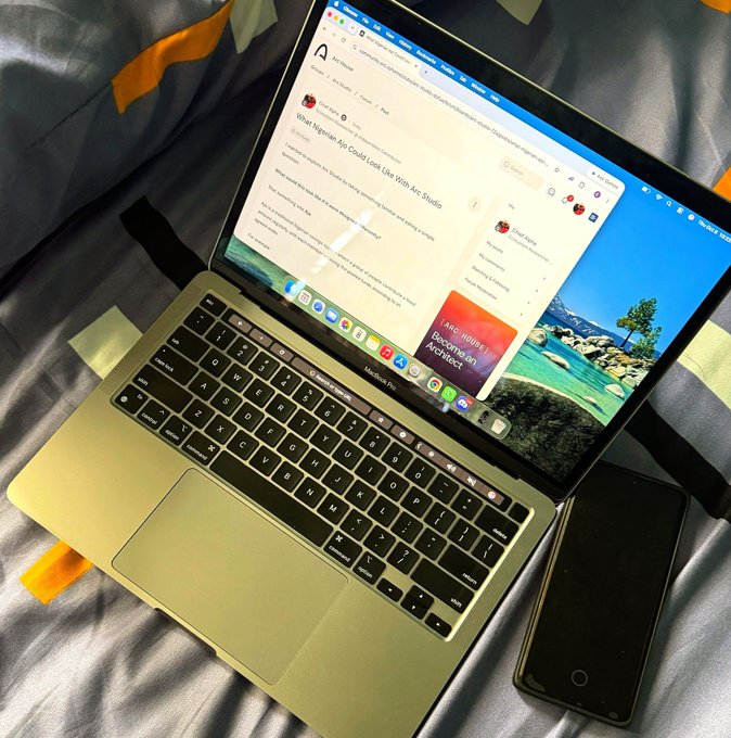 An open MacBook Pro on a bed displaying an article titled 'What Nigerian App Could Look Like With Arc Studio', with an iPhone lying next to it.