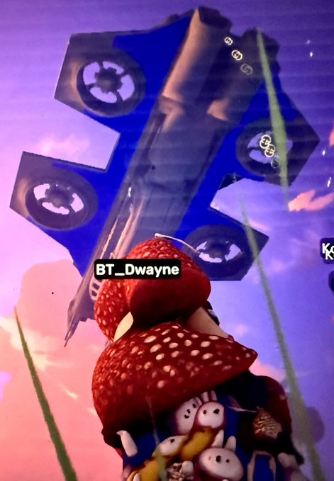 A low-poly video game scene showing a character wearing a strawberry-themed outfit looking up at a large blue flying vehicle, with a player tag reading 'BT_Dwayne'.