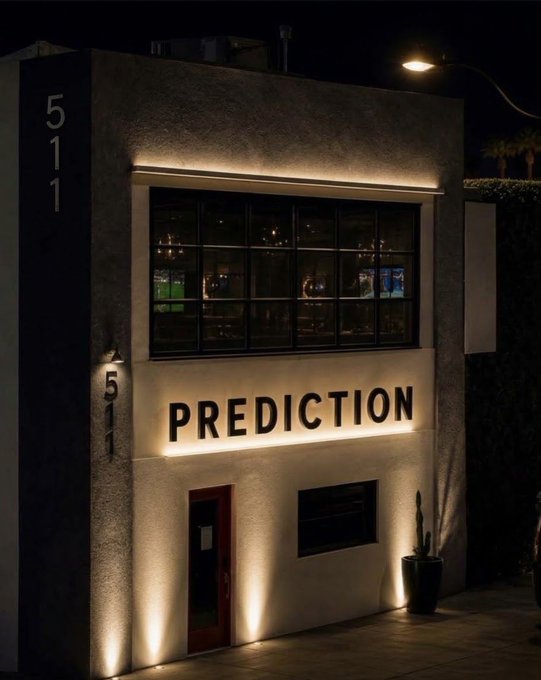 A nighttime photo of a modern building exterior illuminated with lights, featuring a large sign that reads 'PREDICTION' and the address numbers '511' displayed on the facade.