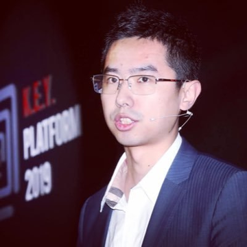 A man with glasses speaks at an event, with a backdrop displaying "R.E.Y. PLATFORM 2019".