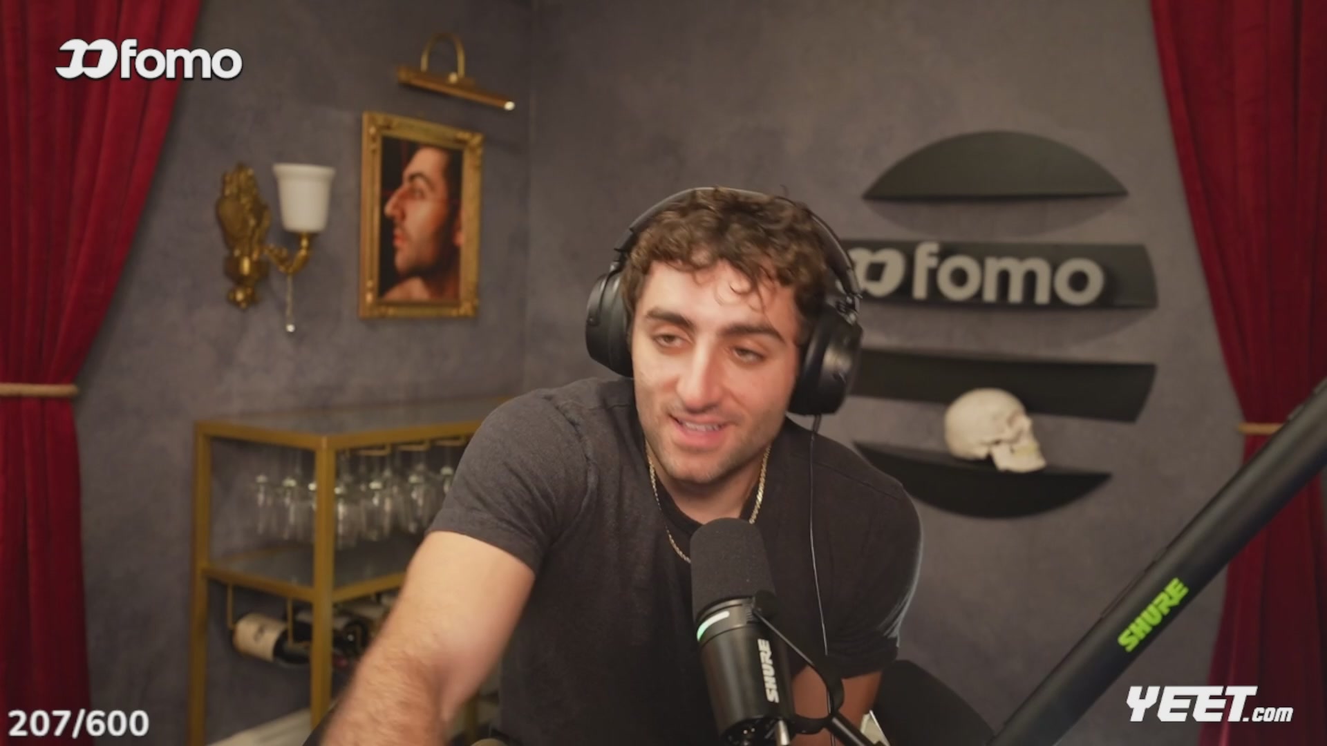 ershman, a man with curly hair and glasses, smiles while holding a microphone at the DFROMO podcast studio, featuring a red curtain backdrop.