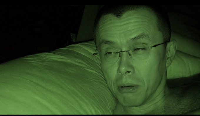 The image, taken with night vision, shows a man wearing glasses lying against a pillow, looking groggy and confused. This captures the disoriented "just woken up" moment referenced in the post, humorously suggesting GM himself appears stunned and unhappy about the rude awakening.