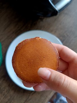 A hand holds a golden-brown pancake over a white plate, playfully visualizing the "PancakeSwap" name from the post. The image humorously relates to the post by literally showing a "pancake" in reference to the PancakeSwap cryptocurrency platform, whose "aggressive stance" likely refers to its recent moves or price action in the crypto market.