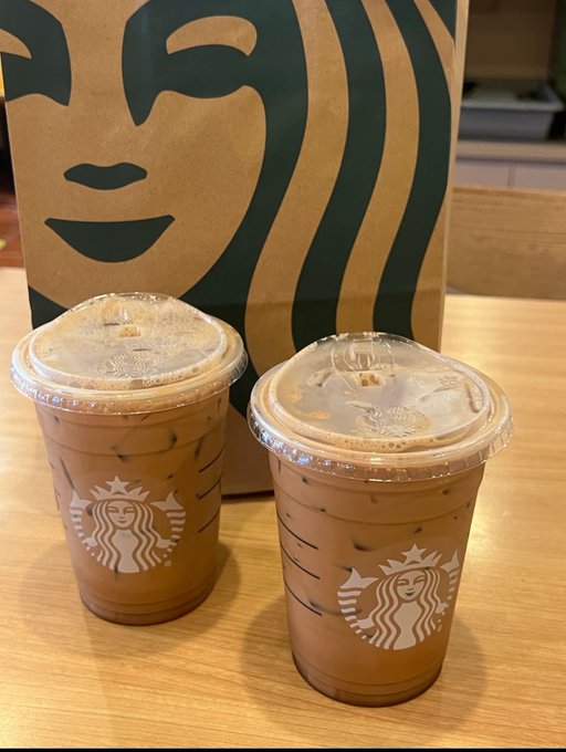 Two iced Starbucks coffee cups sit on a wooden counter in front of a brown Starbucks paper bag. The image accompanies a promotional post from CoinAnk announcing a giveaway with approximately 200 Starbucks drinks remaining, highlighting the platform's data tools for tracking order flows.