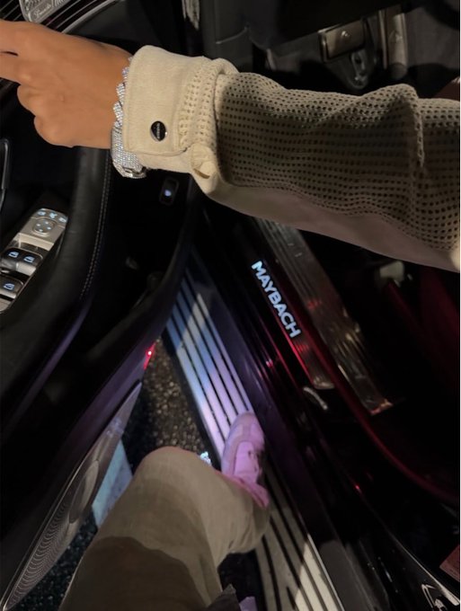 A person steps into a luxury Maybach vehicle, their wrist adorned with a sparkling diamond bracelet as they hold the steering wheel, paired with the post inviting viewers to "like and drop your wallets." The image's display of opulence visually reinforces the post's call to action, suggesting wealth and financial readiness.