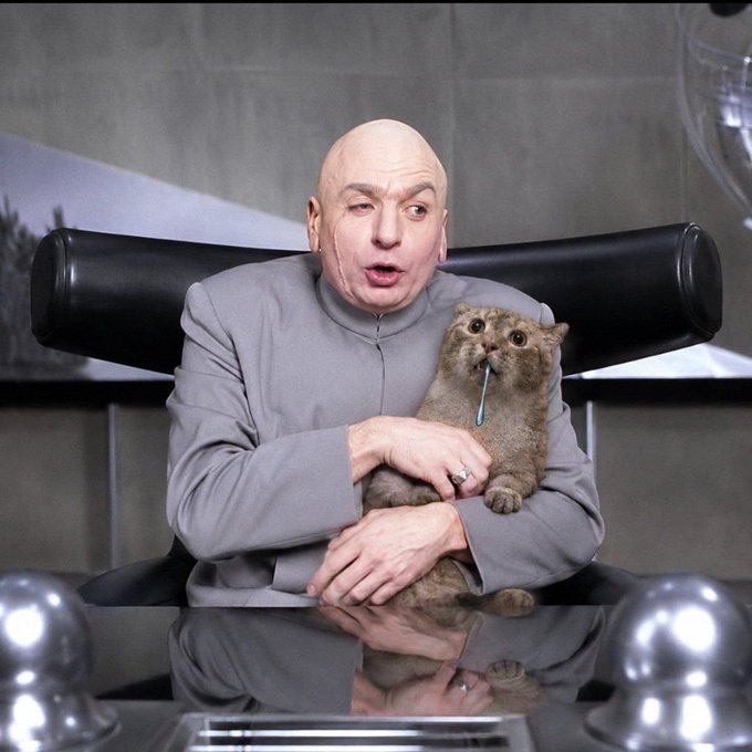 A bald man in a gray high-collar suit sits in a futuristic chair holding a small, wide-eyed creature wearing a collar with an antenna.