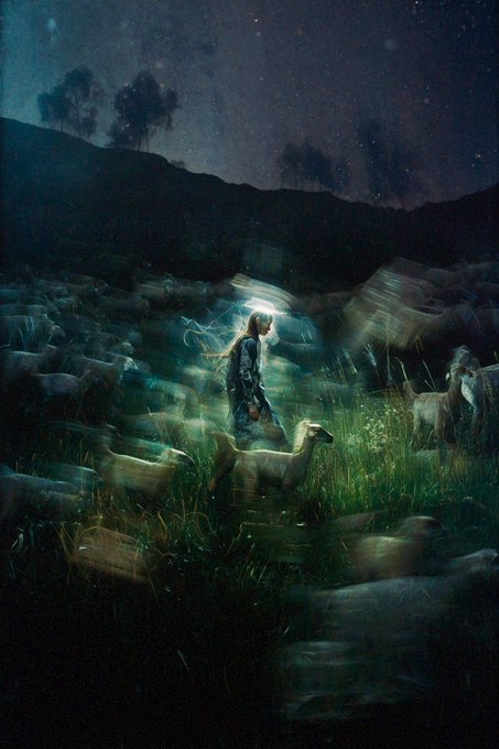 A mystical, dark fantasy illustration shows a solitary figure standing in a grassy field surrounded by a flock of sheep at night, with a glowing aura emanating from them under a starry sky.