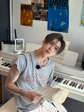 The image features a young man sitting at a piano, holding sheet music while playing the instrument. The photo has been edited with a filter that gives it a "ALPHADRIVEONE" theme. The background of the image includes posters on the wall behind the boy and a TV screen in the room.
