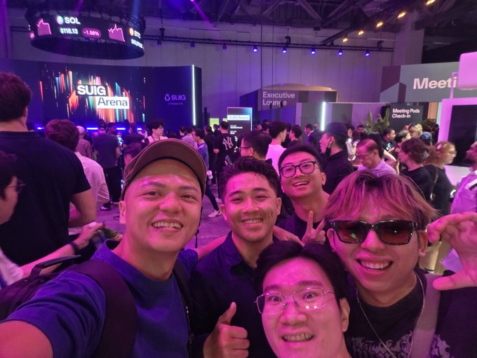 A group of five young men posing for a selfie at the 'SOL Arena' event space, with signs for 'Executive Lounge' and 'Meeting Pods Check-In' visible in the background.