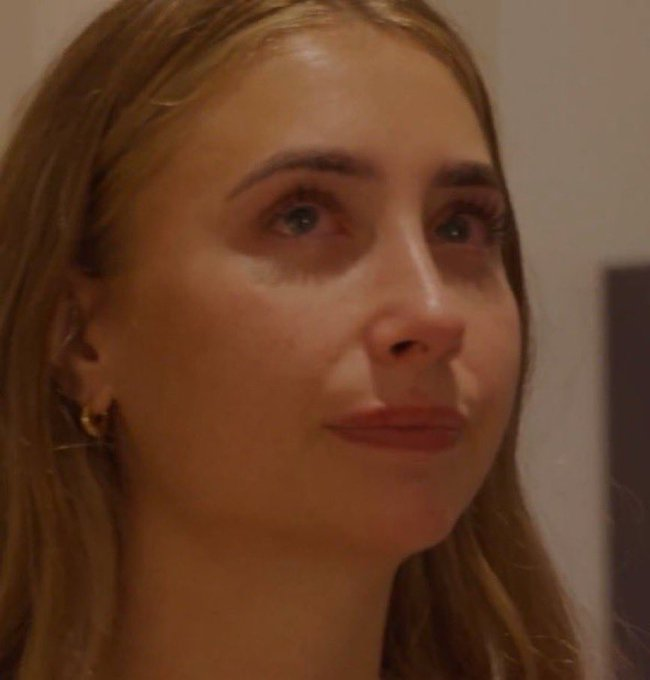 A blonde woman with red eyes stares blankly ahead with a forced neutral expression, embodying the look of someone trying to hide their despair at watching their investment continue to plummet despite "buying the dip."