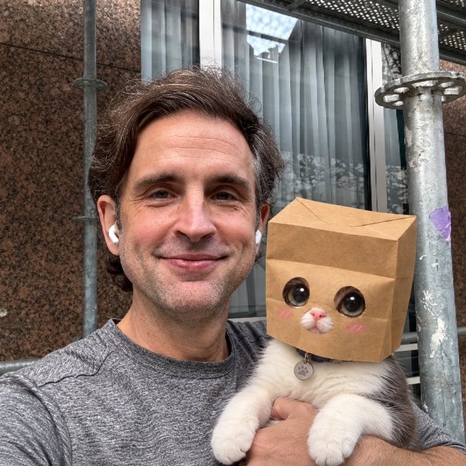 A man smiles while holding a white cat wearing a brown paper bag decorated to look like a cat face with drawn-on eyes and pink cheeks, with no visible text in the image itself. The image doesn't appear to have a direct visual connection to the post about Solana tokens backed by ZEC and ZecHub resources, though the lighthearted nature of the cat photo suggests a casual, community-oriented tone often shared alongside crypto news.