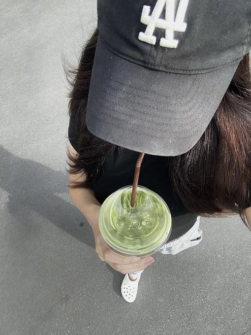 A top-down view of a person wearing a black LA Dodgers cap, drinking a green iced beverage from a plastic cup with a straw.
