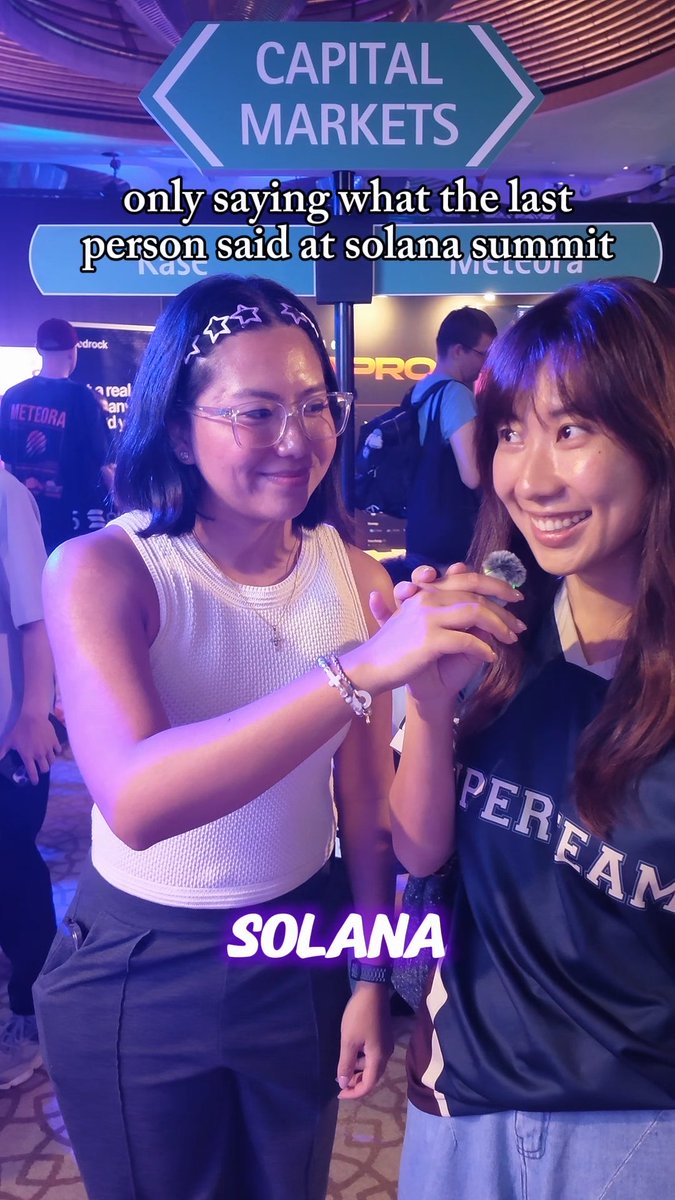 Two young women pose together holding hands at an event with a 'CAPITAL MARKETS' sign behind them, featuring overlay text reading 'only saying what the last person said at solana summit' and 'SOLANA'.