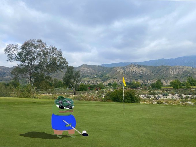 A Pepe the Frog cartoon character, wearing a blue shirt and a tartan tam o' shanter hat, is putting on a golf green with a yellow flag visible in the background, set against mountains.