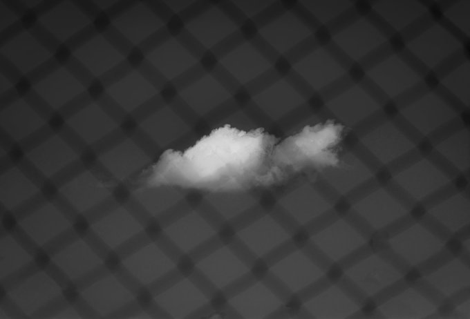 A grayscale image of a small white cloud against a dark checkered pattern background.