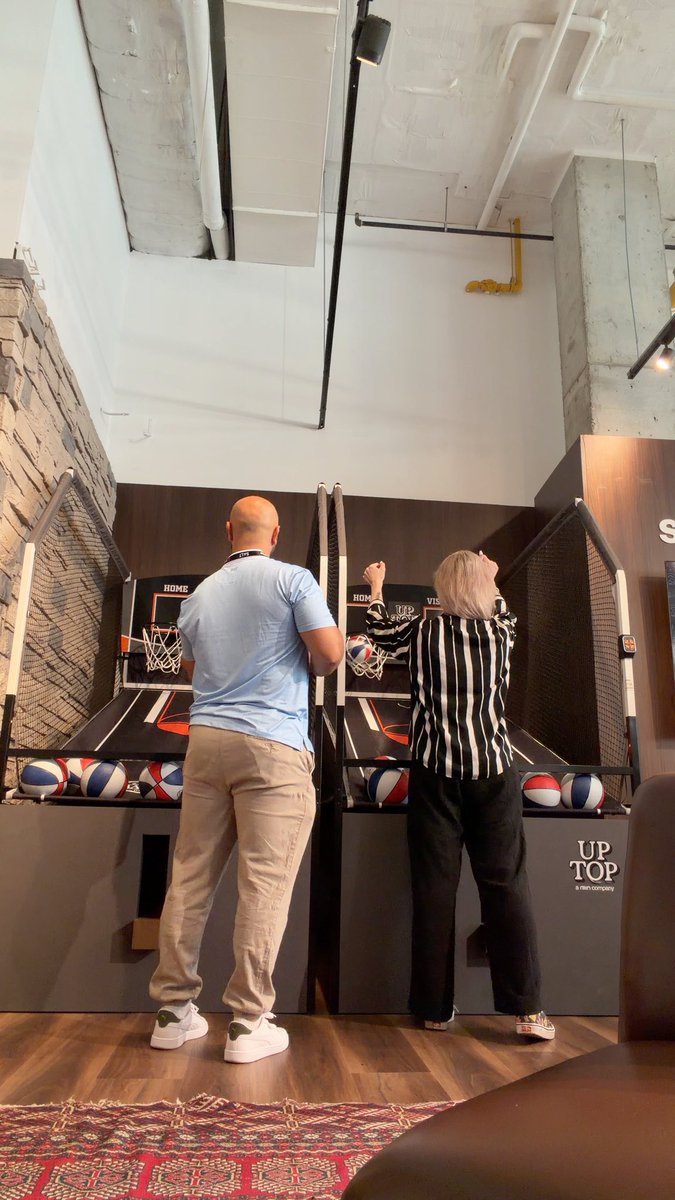 A man in a light blue shirt and a woman in a striped top play a competitive arcade basketball game called 'UP TOP' with balls lined up at the front.