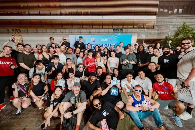 A large group photo of smiling people gathered at a Team Liquid "RESPAWN" event, posing together with branded merchandise.